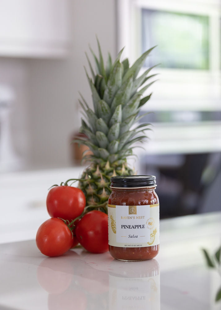 Pineapple Salsa Life Style Photo with Jar on Counter top, tomatoes and pineapple displayed behind the jar
