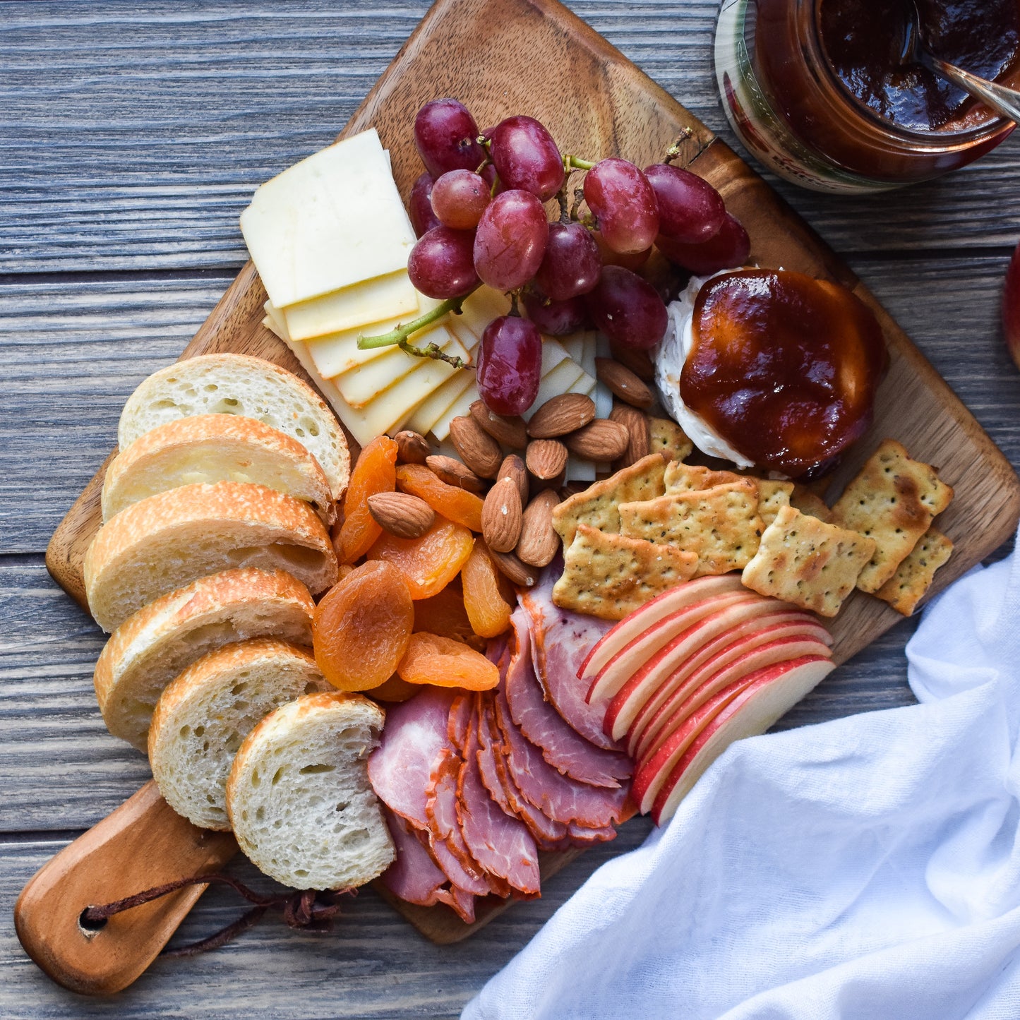 Charcuterie Board with Apple Butter, Apricots, Crackers, Sliced French Bread, Grapes, Cheese, and Cured Meats