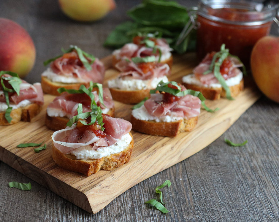 Crostini appetizer topped with ricotta, peach salsa, prosciutto, and basil