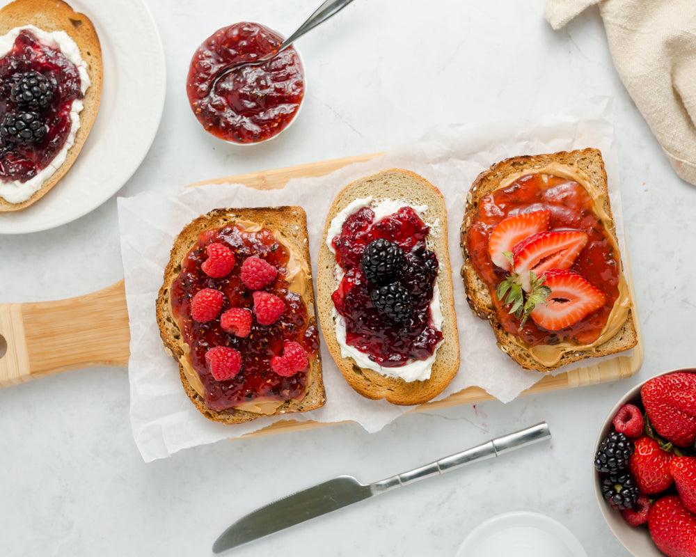 Three slices of toast on wooden board topped with jams and berries