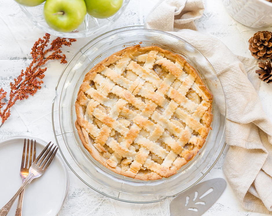 Apple pie made with Raven's Nest mulling spice surrounded by fresh granny smith apples and fall foliage with a lattice top crust
