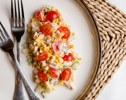 Charred corn salad with tomatoes and onions made with Raven's Nest garden party mix served on a plate with 2 forks