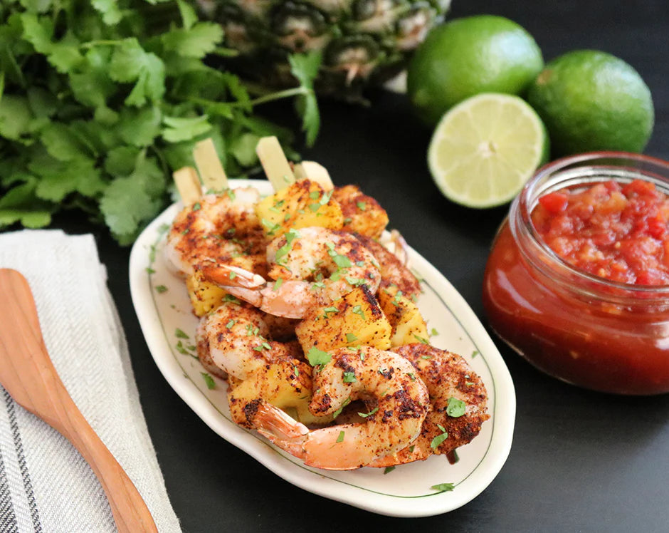 Grilled shrimp and pineapple skewers with a side of pineapple salsa, cilantro, and lime wedges