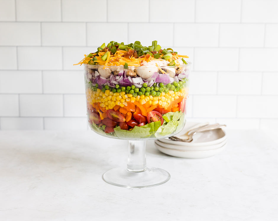 Layered salad with tomatoes, bell peppers, corn, peas, onions, mushrooms, cheese, and more topped with Raven's Garden Party dressing