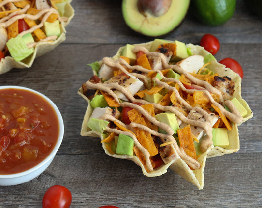 Taco salad in tortilla bowl topped with Raven's Nest chili grande seasoned chicken, tortilla strips, and avocado with a side of mango salsa