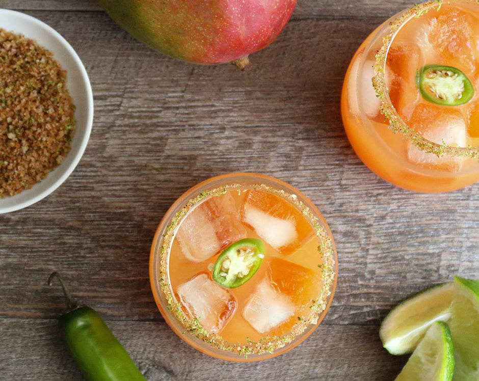 Mango habanero margarita cocktail garnished with limes and jalapenos with a salt and pepper rim