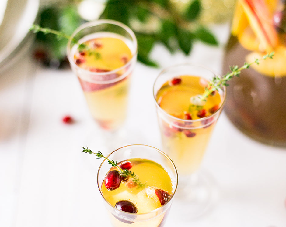 Sparkling winter sangria cocktail recipe made with Raven's Nest mulling spice for a New Years Eve party garnished with fresh herbs, apples, and cranberries
