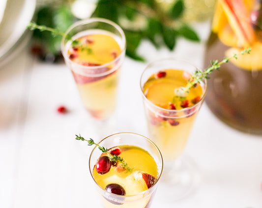 Sparkling winter sangria cocktail recipe made with Raven's Nest mulling spice for a New Years Eve party garnished with fresh herbs, apples, and cranberries