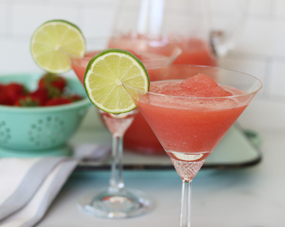 Two martini glasses with strawberry jalapeno jam daiquiris garnished with limes